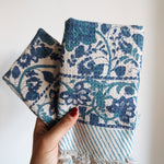 Hand holding two blue floral patterned fabric napkins with a white background