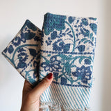 Hand holding two blue floral patterned fabric napkins with a white background