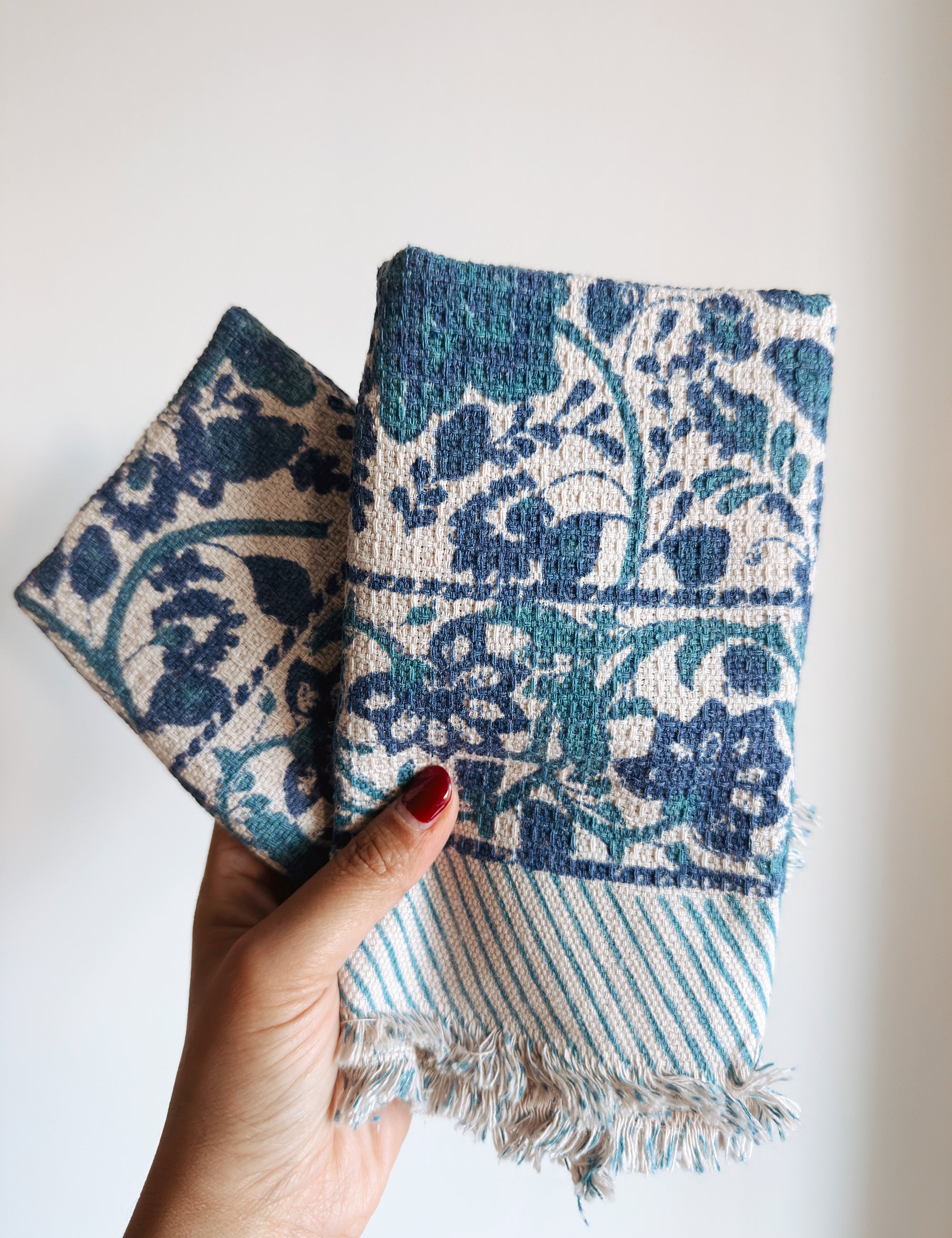 Hand holding two blue floral patterned fabric napkins with a white background