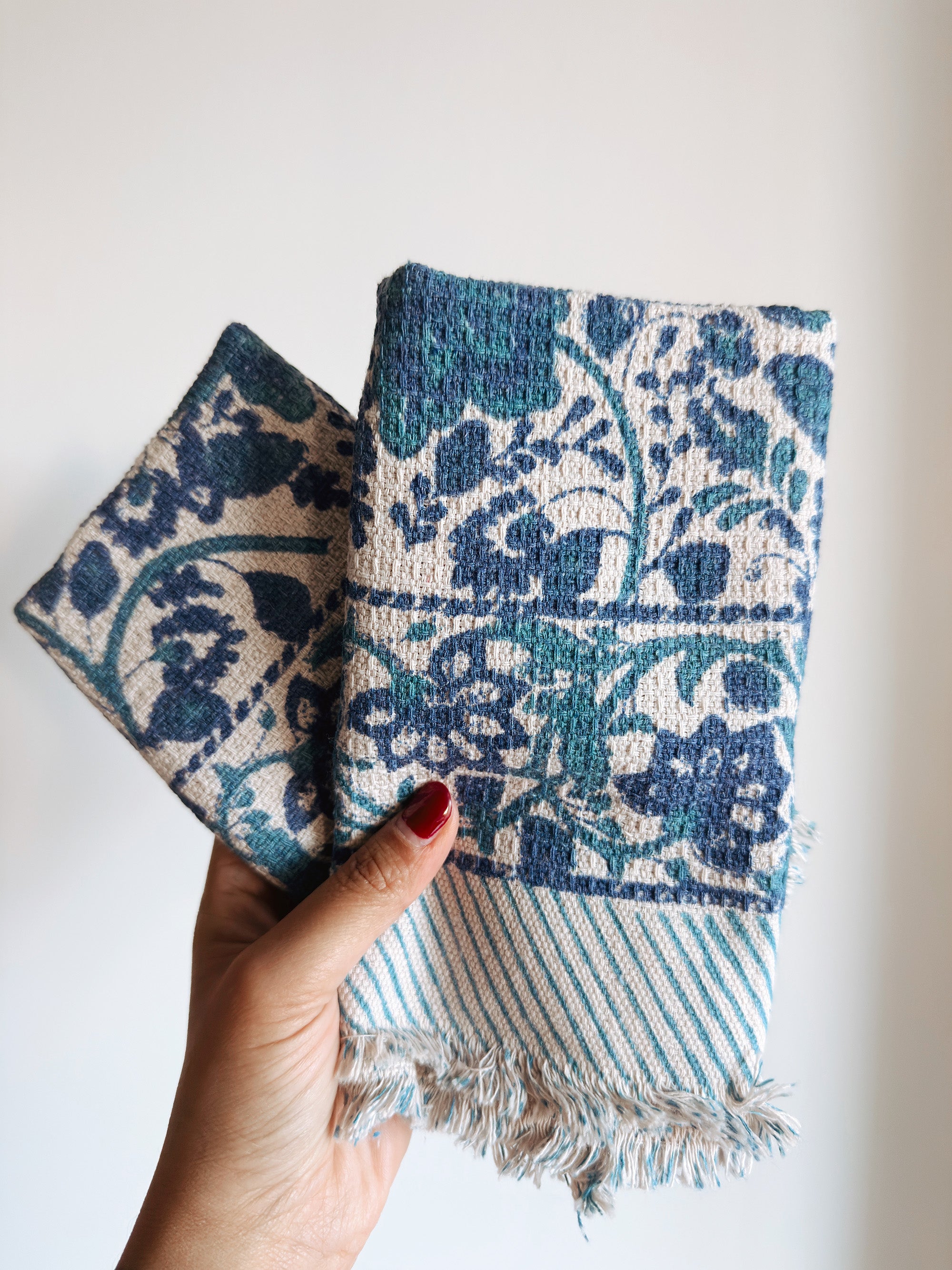 Hand holding two blue floral patterned fabric napkins with a white background