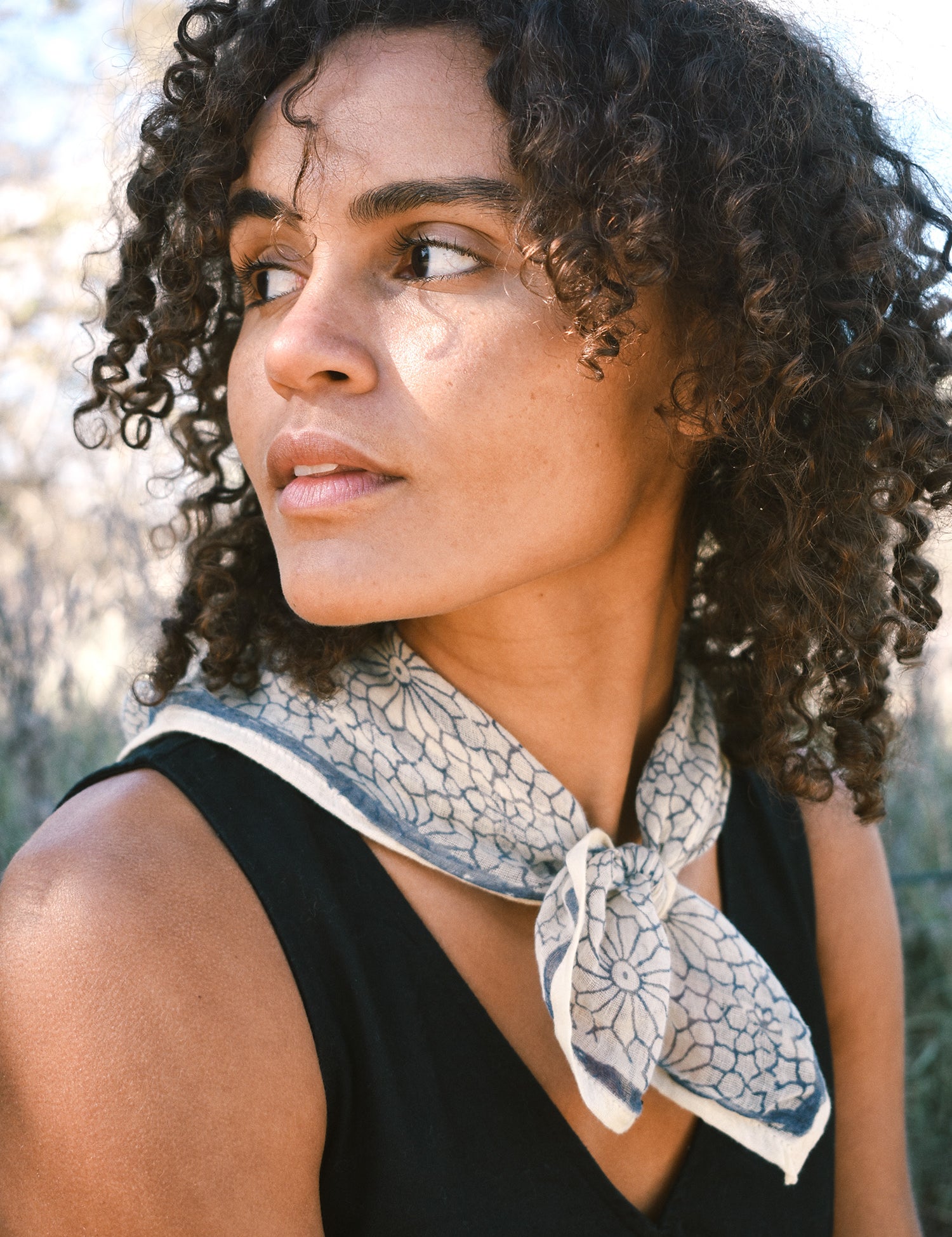 Woman wearing block print Mosaic bandana tied around neck against a black sleeveless dress.