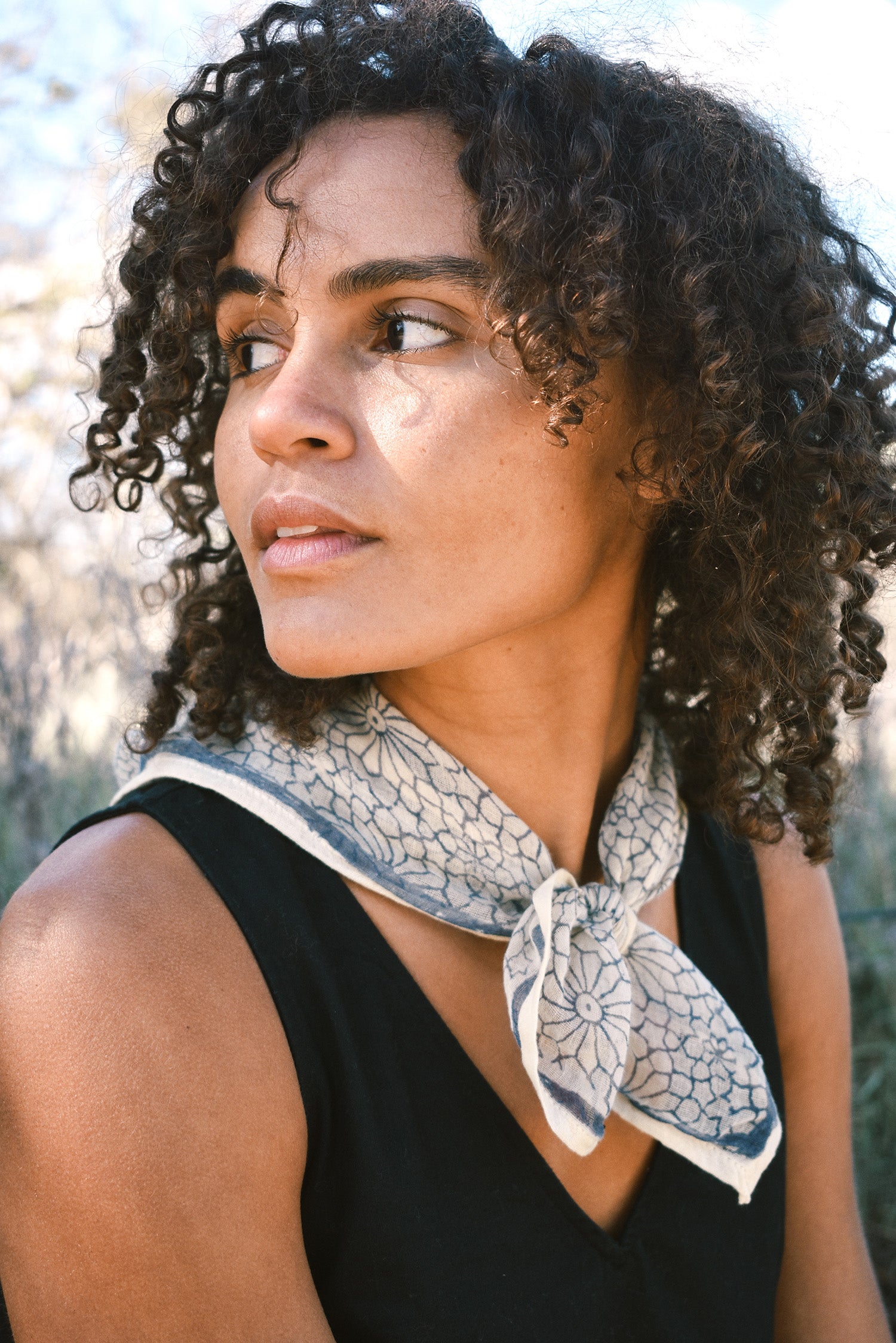 Woman wearing block print Mosaic bandana tied around neck against a black sleeveless dress.