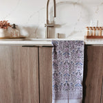 Kitchen sink area with a purple floral towel hanging on a wooden cabinet.