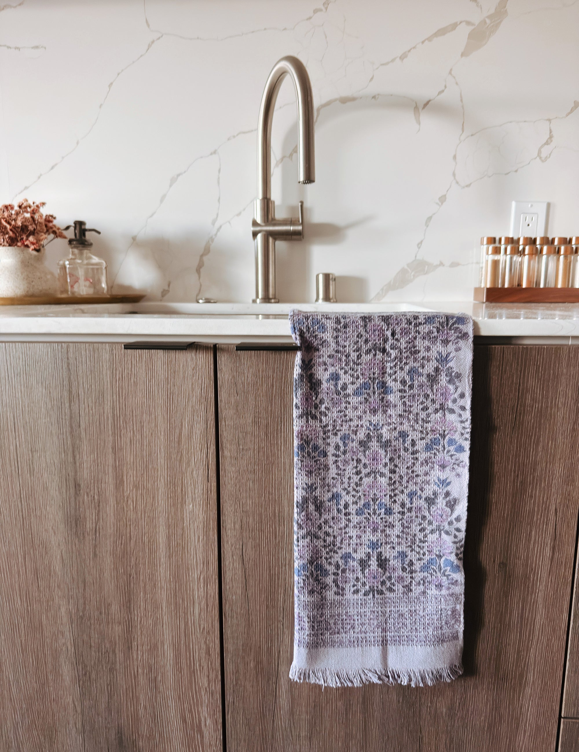 Kitchen sink area with a purple floral towel hanging on a wooden cabinet.