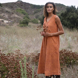 Model standing in a field, holding flowers, wearing the Stevie sleeveless orange block printed corduroy jumpsuit