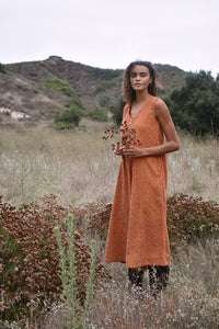 Model standing in a field, holding flowers, wearing the Stevie sleeveless orange block printed corduroy jumpsuit
