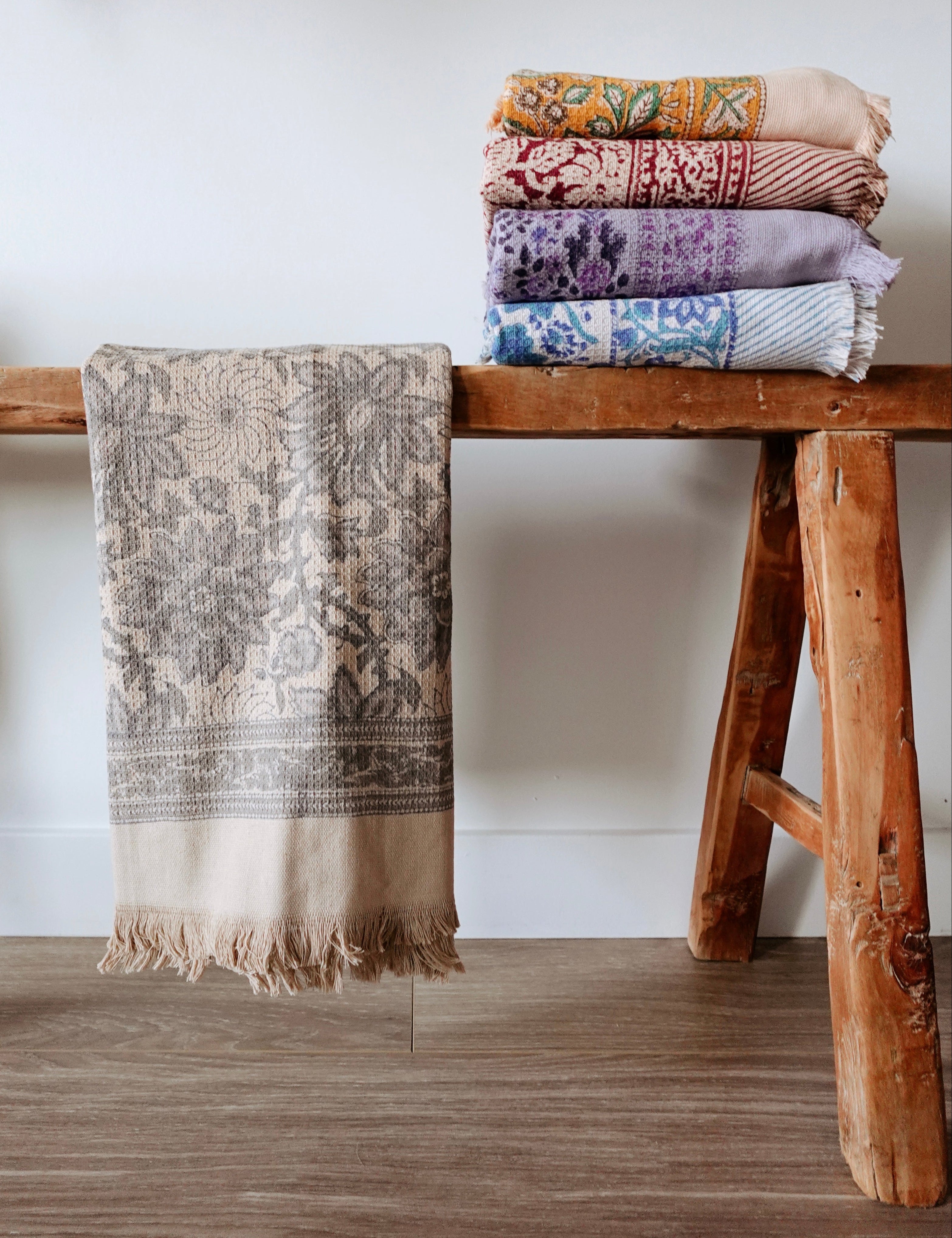 Stack of patterned towels on a wooden bench against a white wall.