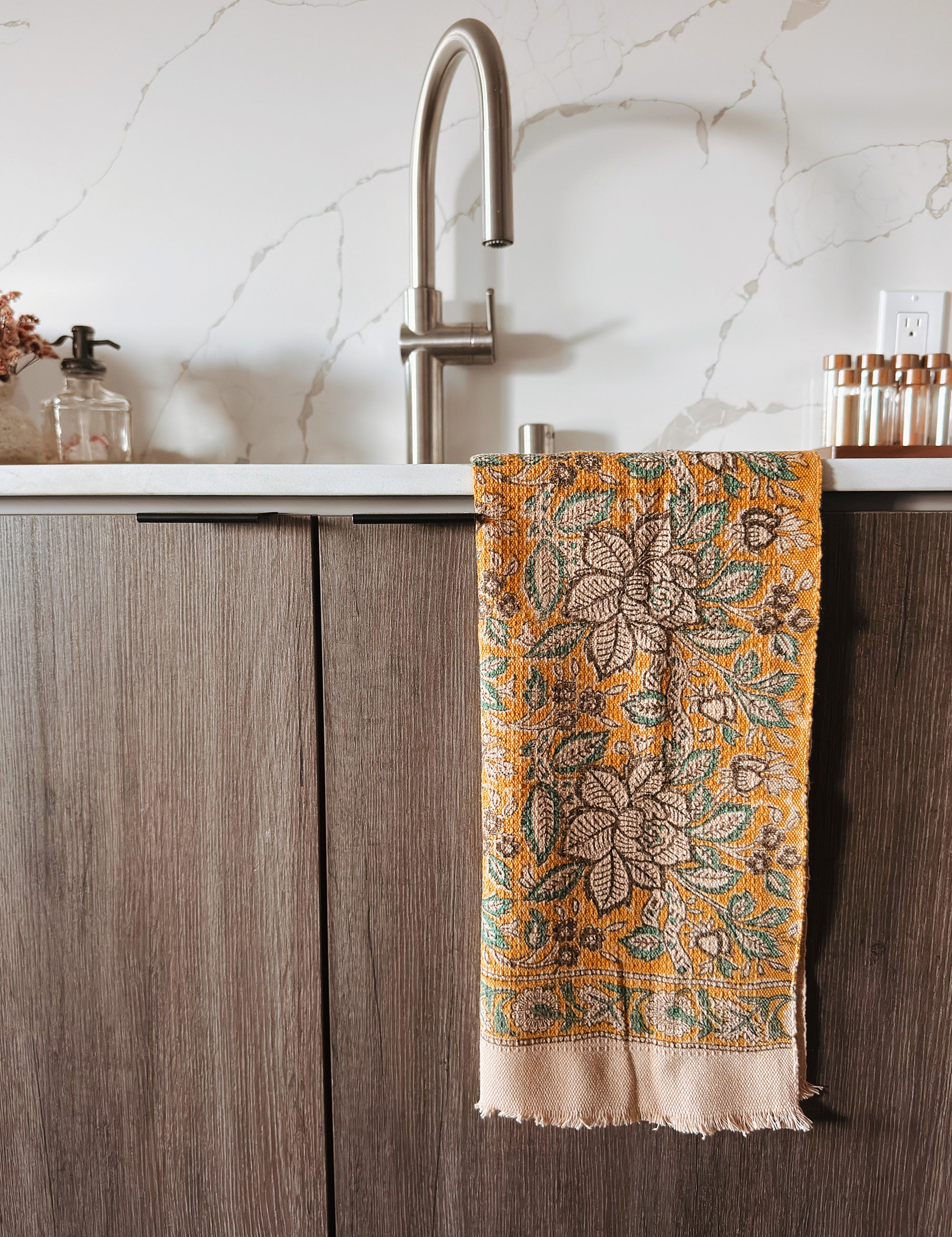 Decorative floral towel hanging on a kitchen cabinet with a marble backsplash.