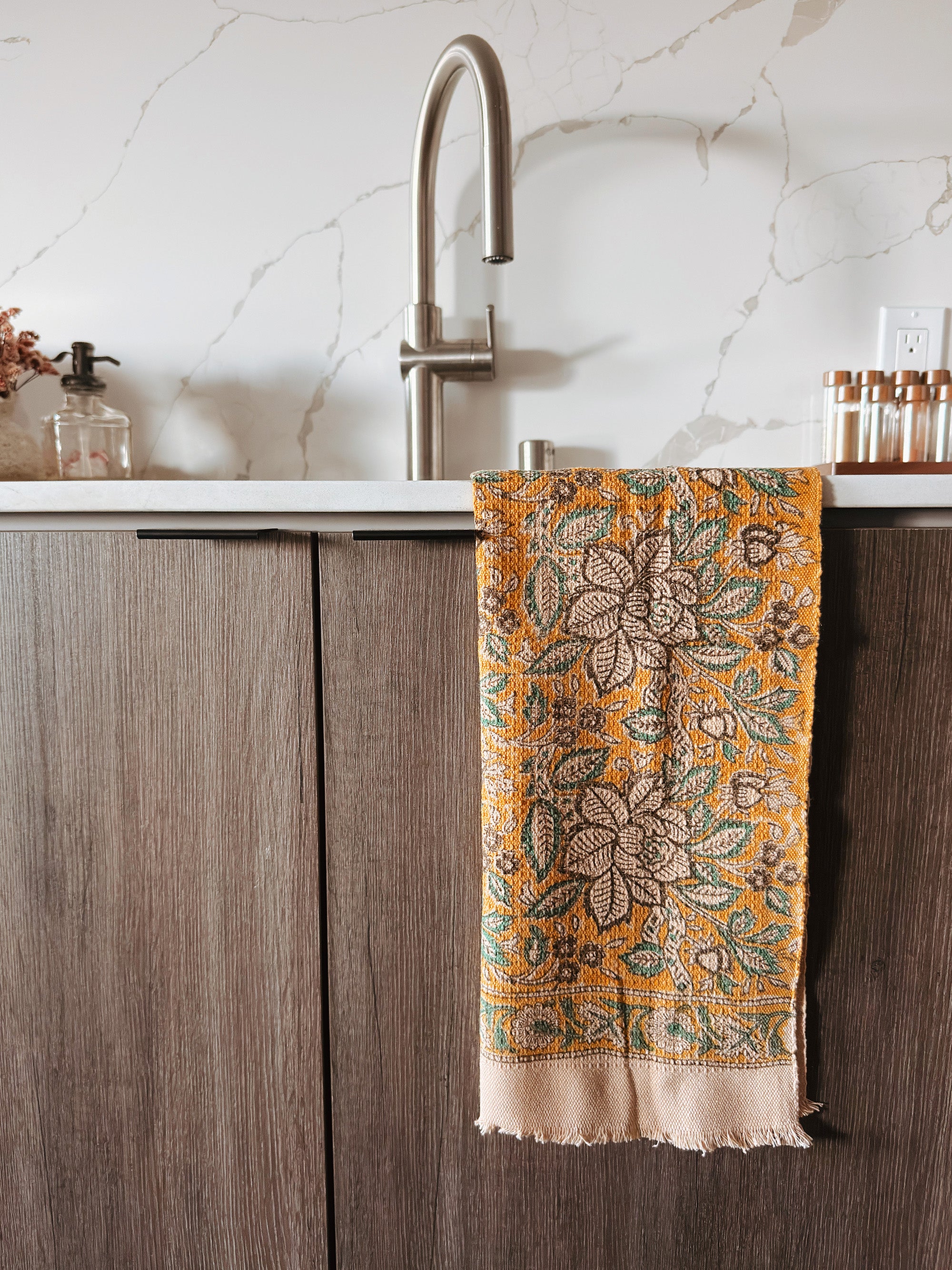 Decorative floral towel hanging on a kitchen cabinet with a marble backsplash.