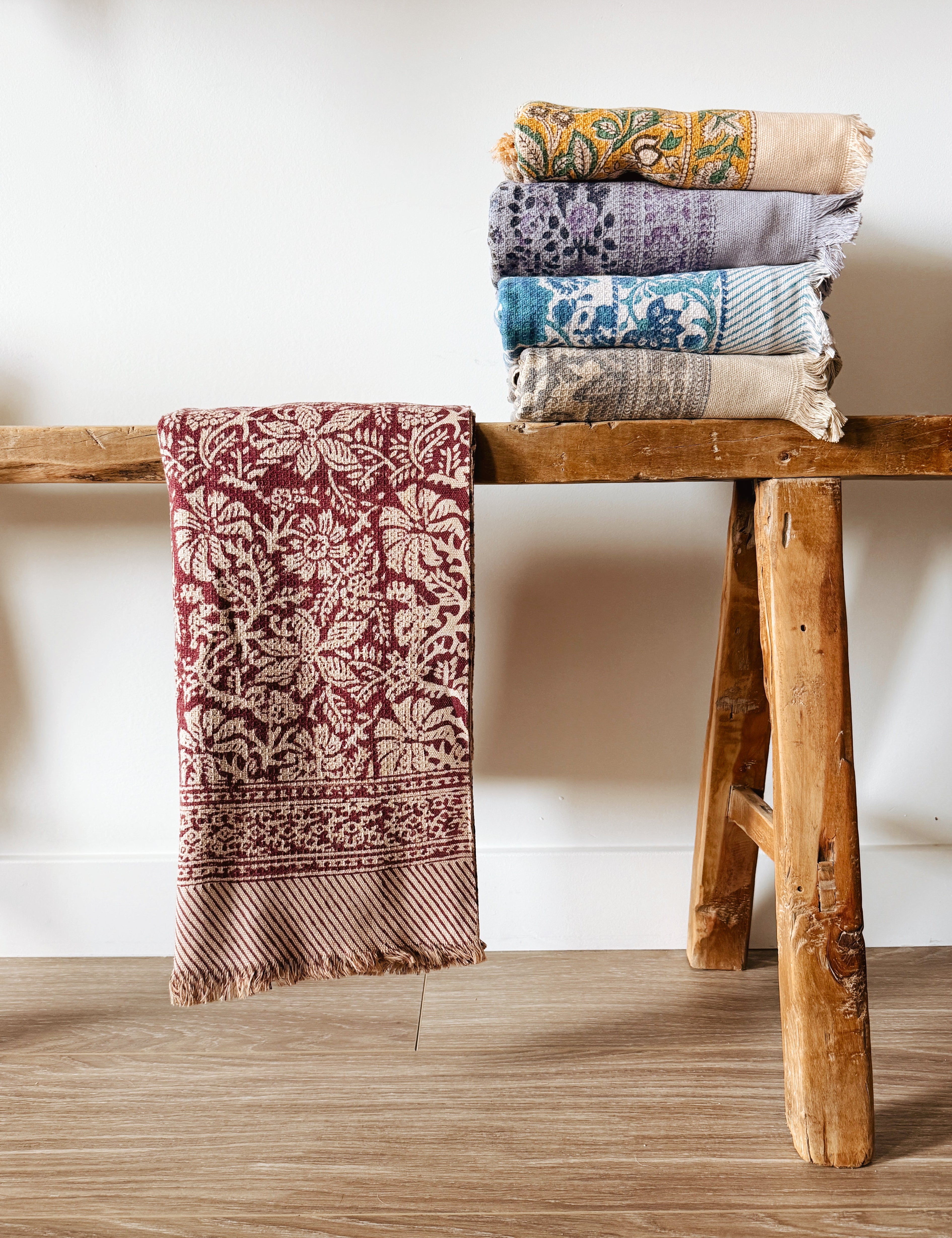 Stack of floral printed bath towels on a wooden stool against a white wall