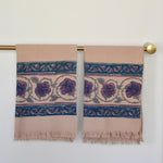 Block printed Lilac Khadi hand towels hanging on a golden rod. Towels have a large floral border print. 