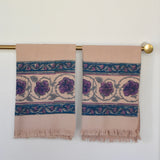 Block printed Lilac Khadi hand towels hanging on a golden rod. Towels have a large floral border print. 