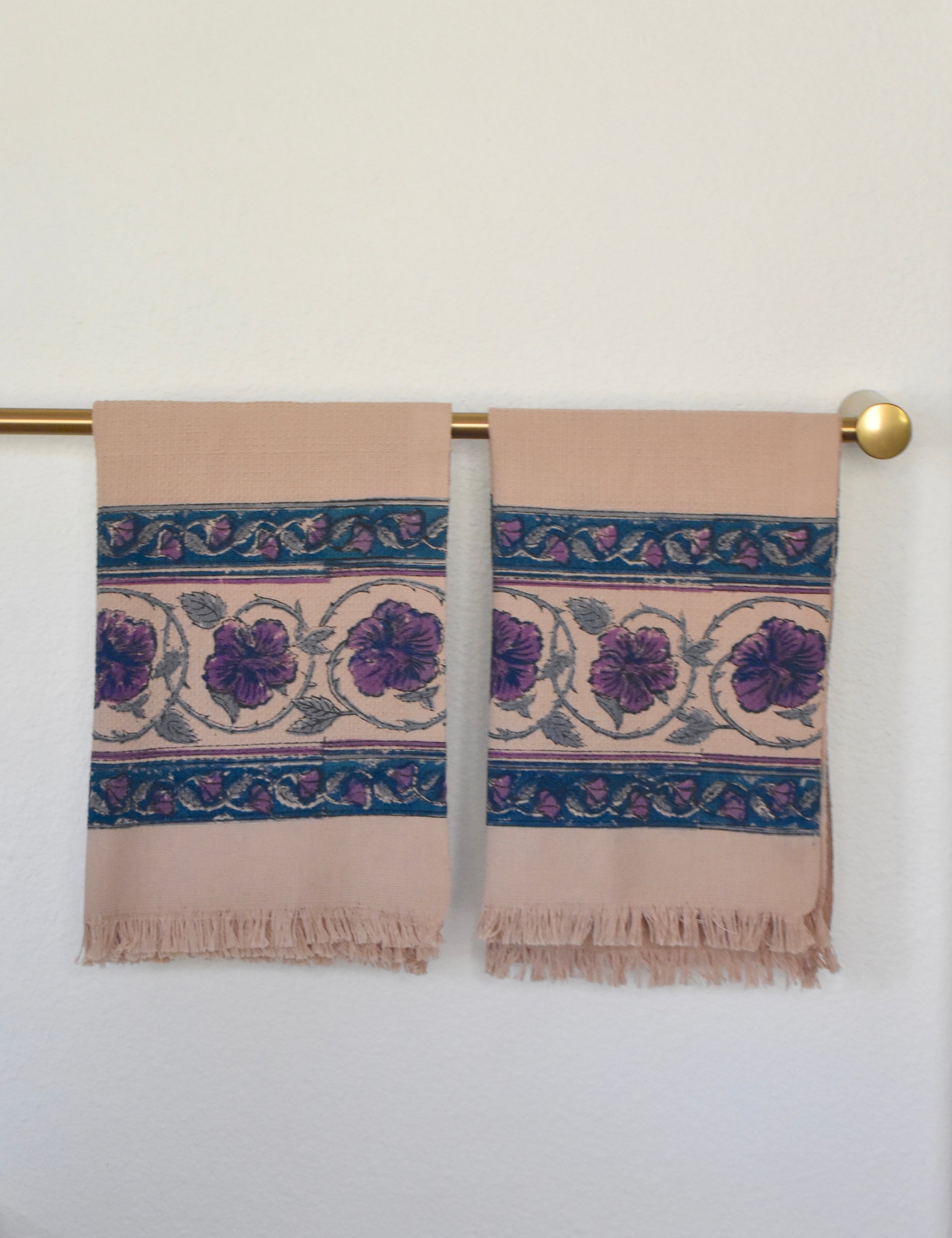 Block printed Lilac Khadi hand towels hanging on a golden rod. Towels have a large floral border print. 