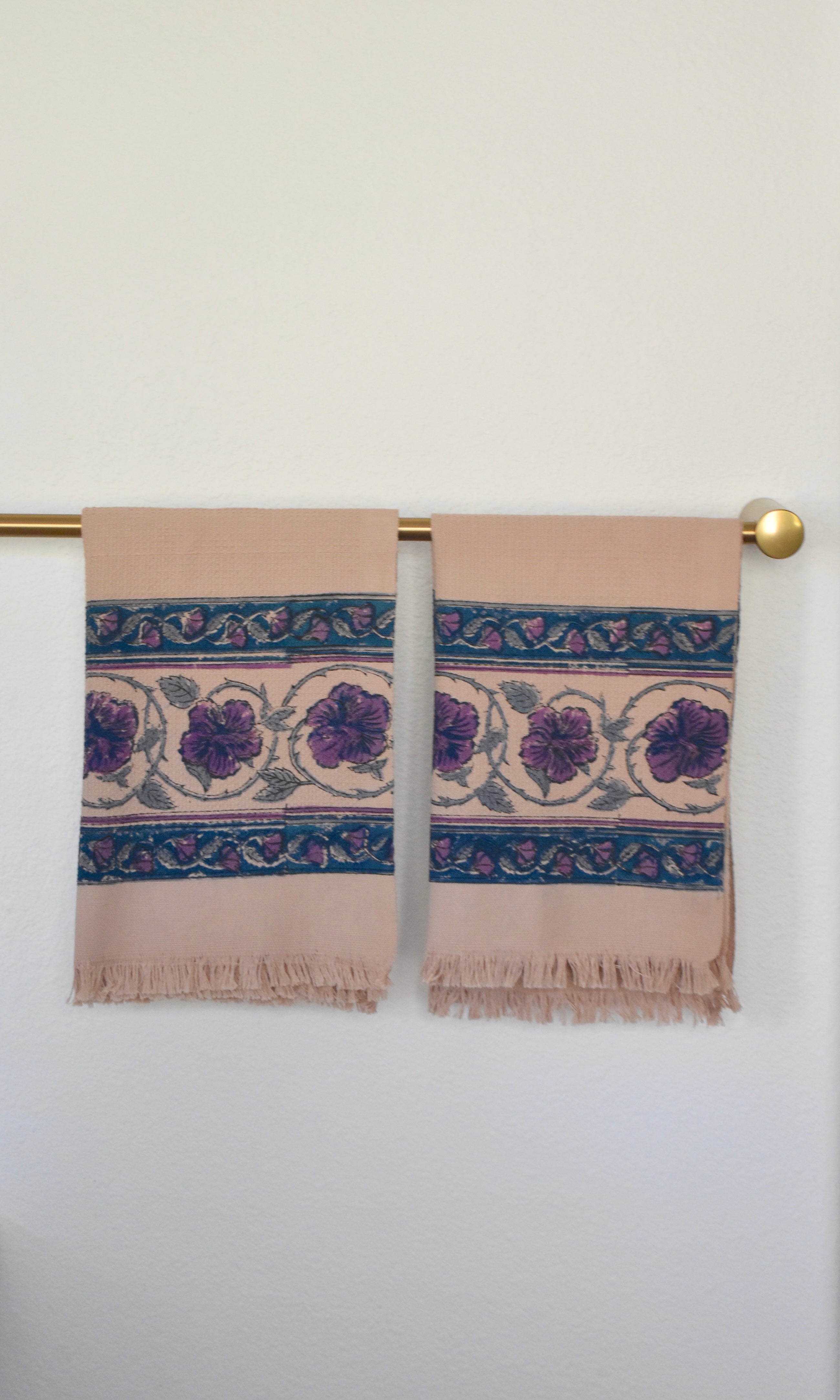 Block printed Lilac Khadi hand towels hanging on a golden rod. Towels have a large floral border print. 