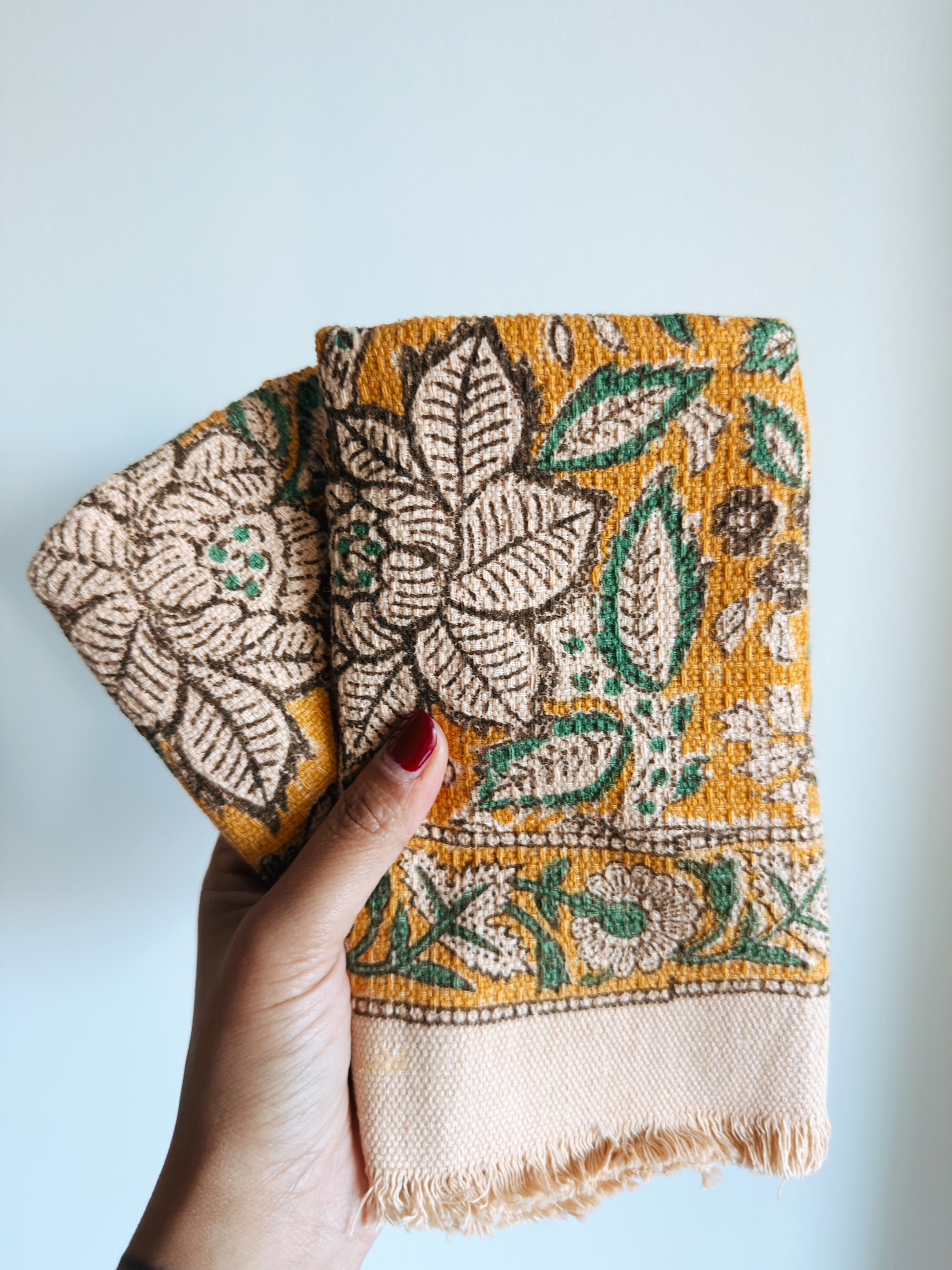 Hand holding folded towels with floral pattern against a plain background