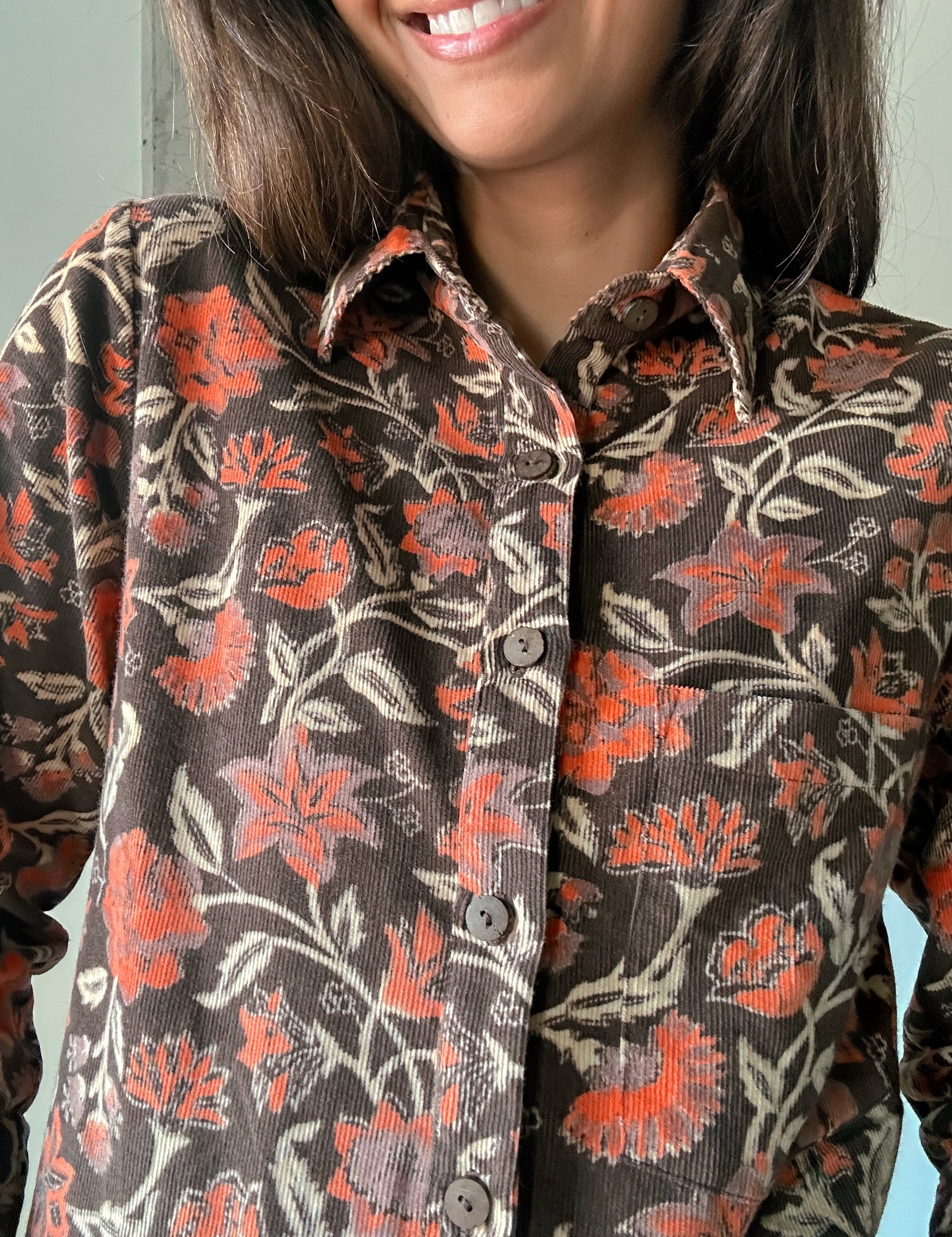 Close up of block printed, brown corduroy shirt with orange and beige flowers. Shirt has one breast pocket.