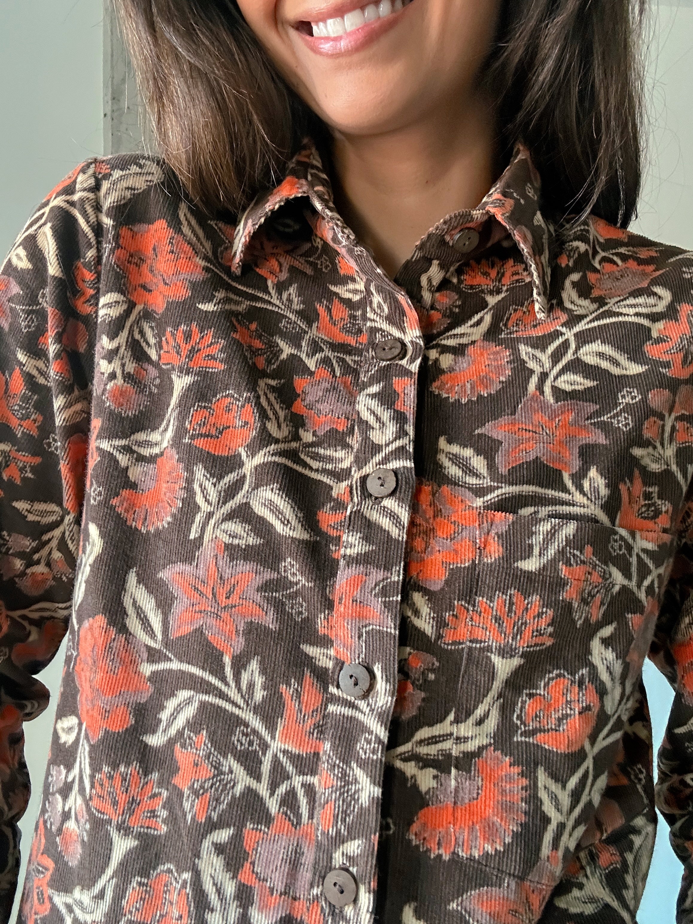 Close up of block printed, brown corduroy shirt with orange and beige flowers. Shirt has one breast pocket.