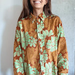 Woman wearing an orange and red corduroy floral shirt with green flowers against a plain background