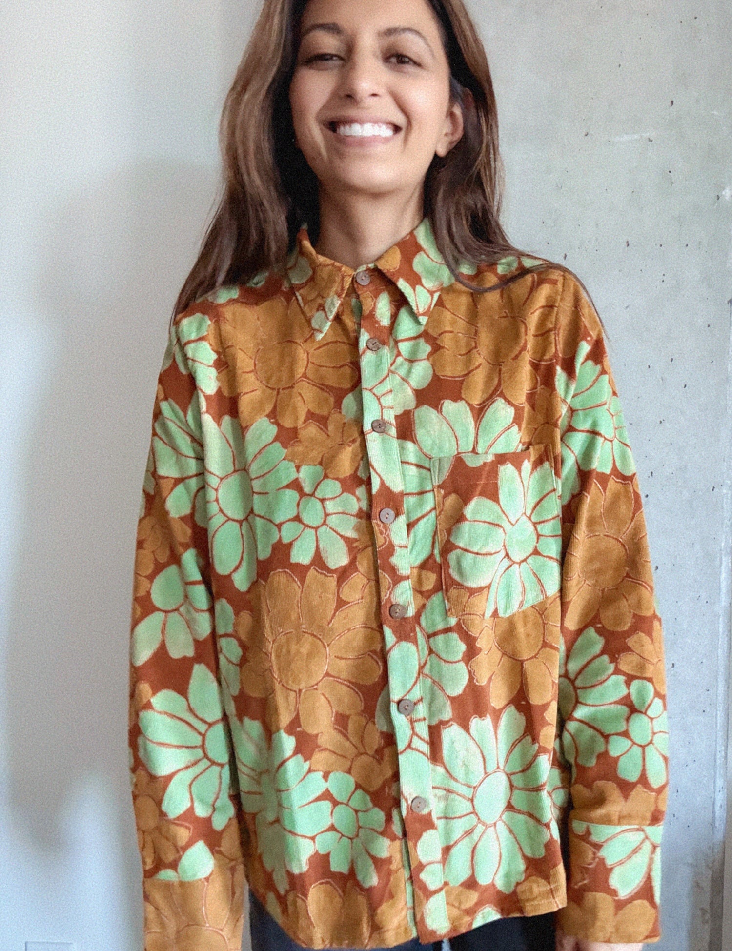 Woman wearing an orange and red corduroy floral shirt with green flowers against a plain background