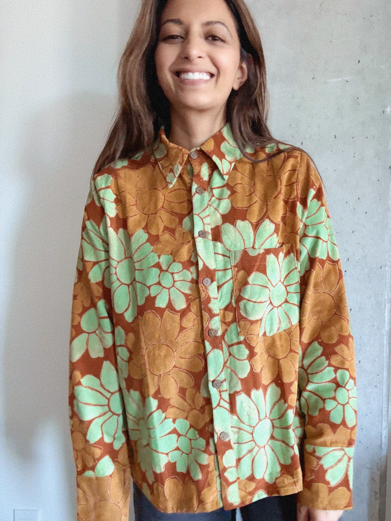Woman wearing an orange and red corduroy floral shirt with green flowers against a plain background