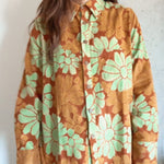 Woman wearing an orange and red corduroy floral shirt with green flowers against a plain background