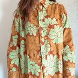 Woman wearing an orange and red corduroy floral shirt with green flowers against a plain background