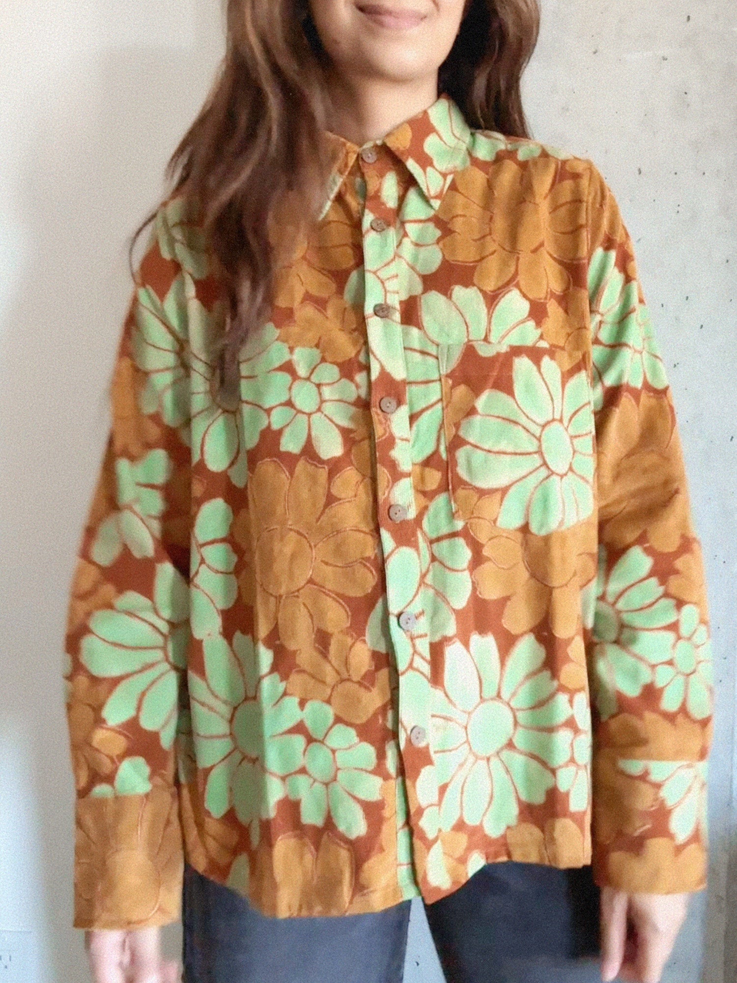 Woman wearing an orange and red corduroy floral shirt with green flowers against a plain background