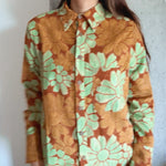 Person wearing a floral patterned shirt with green and orange colors against a plain background