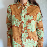 Person wearing a floral patterned shirt with green and orange colors against a plain background