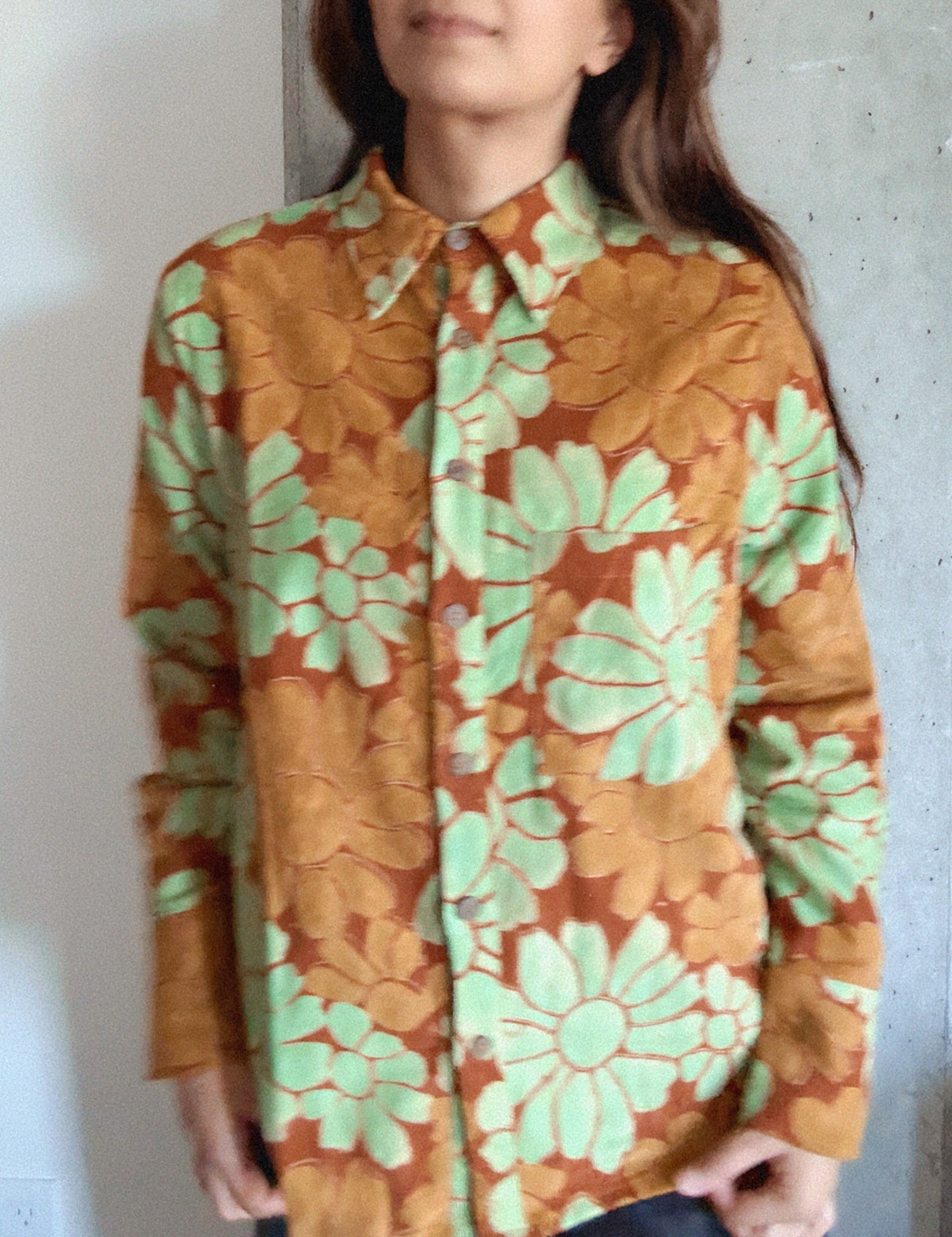 Person wearing a floral patterned shirt with green and orange colors against a plain background