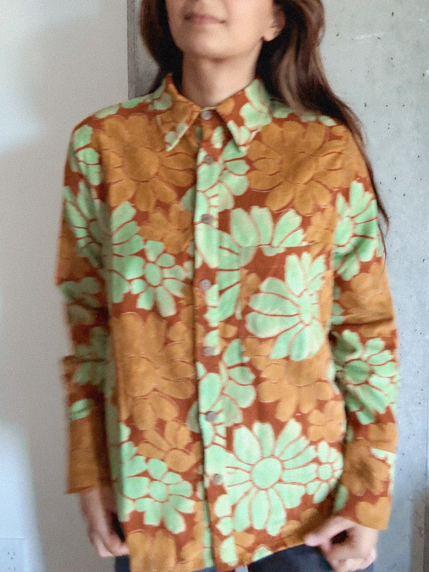 Person wearing a floral patterned shirt with green and orange colors against a plain background