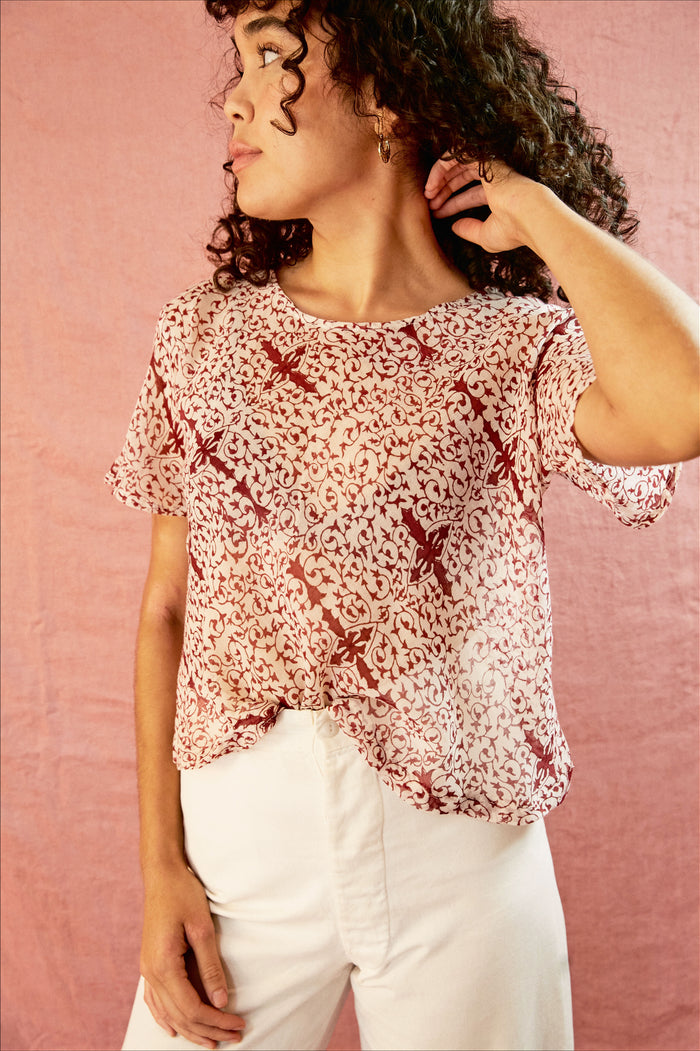 Model wearing the Alicia Top with white pants, against a pink backdrop.