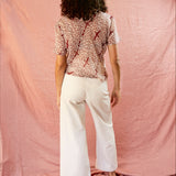 Model wearing the Alicia Top with white pants, against a pink backdrop. Backside of model.