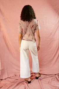 Model wearing the Alicia Top with white pants, against a pink backdrop. Backside of model.