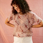 Model wearing the Alicia Top with white pants, against a pink backdrop.