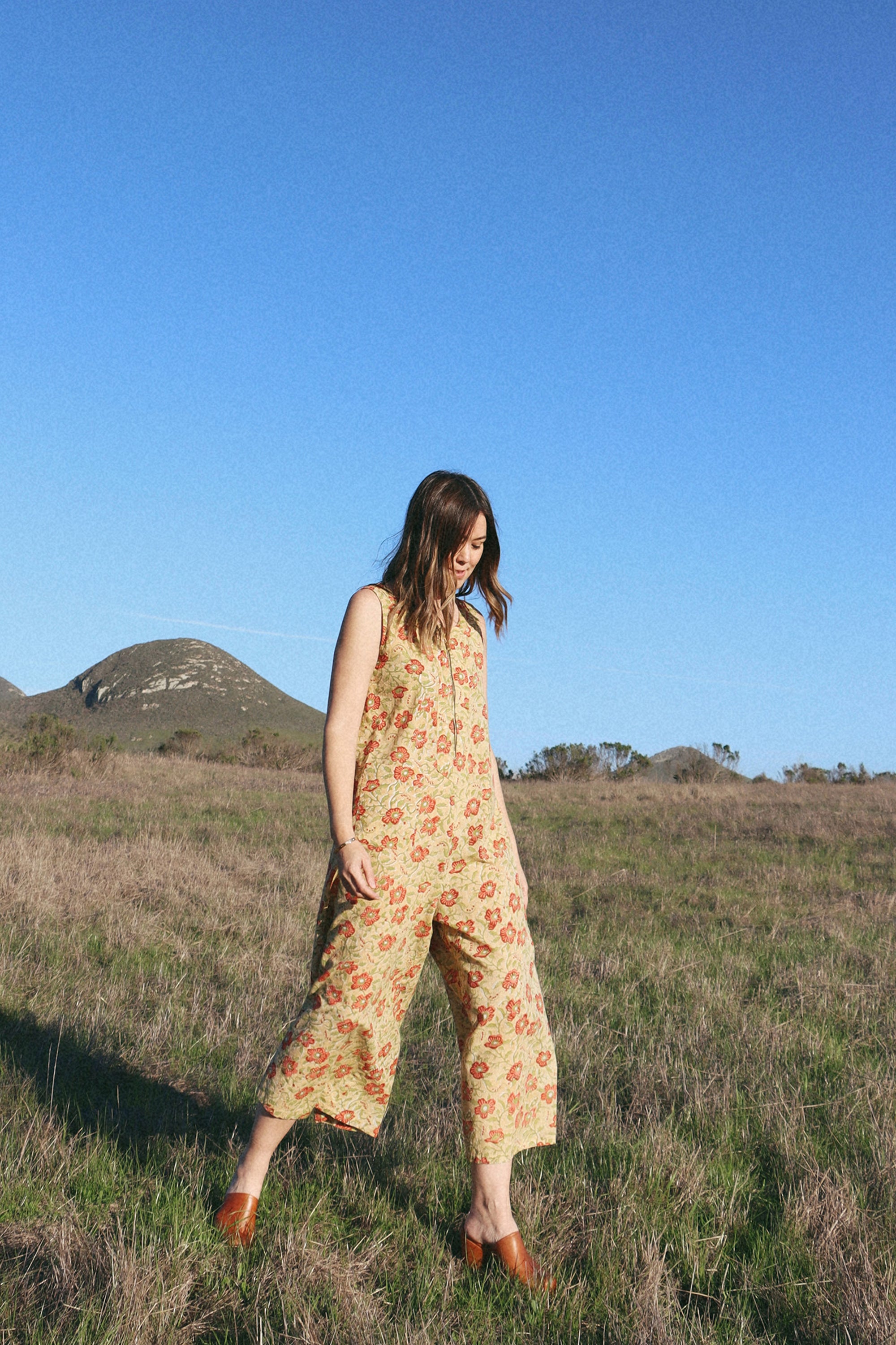 Woman wearing our new block printed floral print cotton sleeveless jumpsuit outside with hills in the background