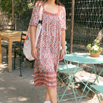 Woman is wearing the Mia dress outside next to a table and in front of trees. Model is wearing converse and a tote bag on her shoulder.