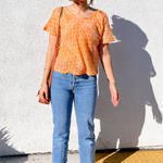 Woman is wearing the Sophie Crop Top with a cropped pair of jeans, sandals and a purse. Against a white wall.